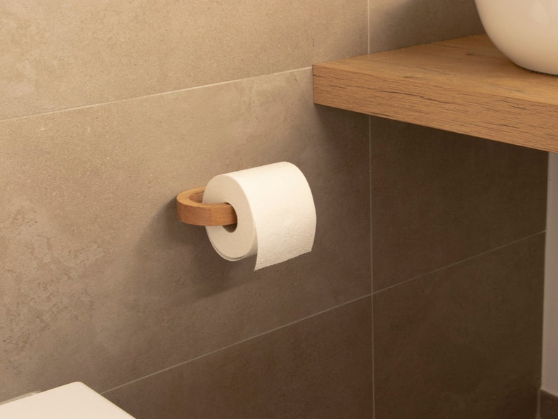 May include: A white toilet paper roll on a wooden toilet paper holder mounted on a beige tiled wall.