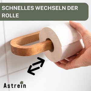 May include: A wooden toilet paper holder with a white toilet paper roll. The holder has a unique design that allows for easy changing of the roll. The text "SCHNELLES WECHSELN DER ROLLE" is visible in the image.