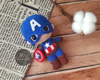 May include: A crocheted amigurumi doll of Captain America. The doll is wearing a blue and red costume with a white star on the chest. The doll is holding a red, white, and blue shield.