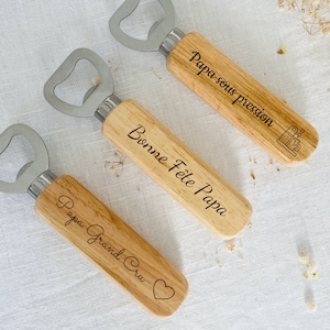 May include: Three wooden bottle openers with engraved messages. The first opener says "Papa sous pression" with a small coffee maker icon. The second opener says "Bonne F&ecirc;te Papa". The third opener says "Papa Grand Cru" with a heart icon.