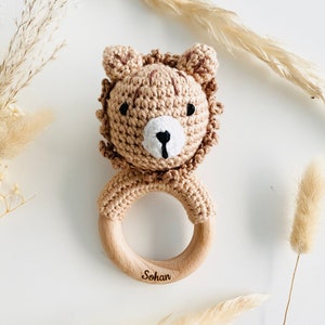 May include: A brown crocheted lion rattle with a wooden ring. The ring is engraved with the name "Sohan".