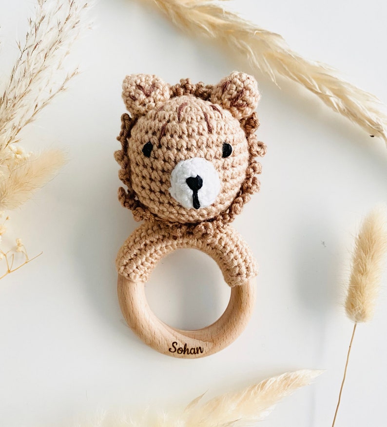 May include: A brown crocheted lion rattle with a wooden ring. The ring is engraved with the name "Sohan".