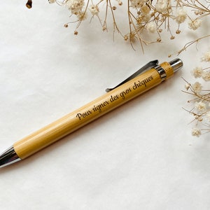 以下が含まれることがあります： 銀色のクリップと「Pour signer des gros chèques」という黒い文字が刻まれた竹製のペンです。
