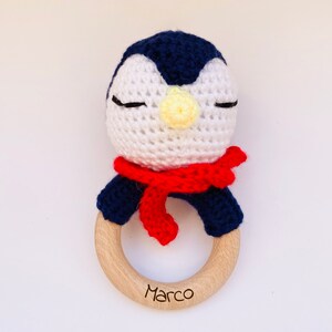 May include: A crocheted penguin rattle with a red scarf and a wooden ring with the name "Marco" engraved on it.