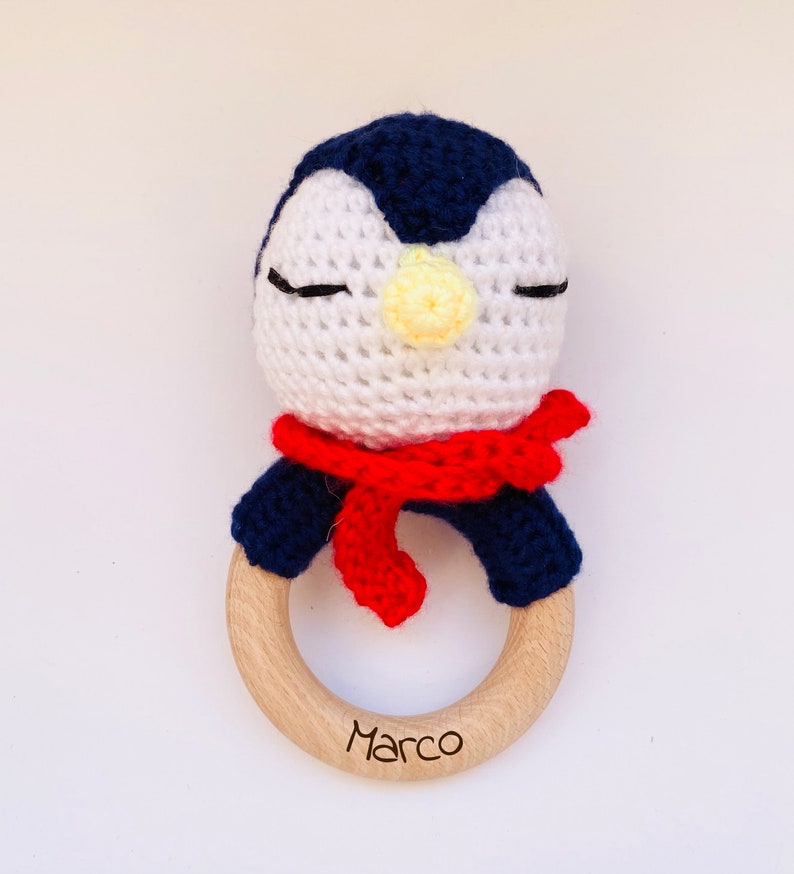 May include: A crocheted penguin rattle with a red scarf and a wooden ring with the name "Marco" engraved on it.