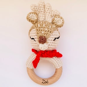 May include: A crocheted deer rattle with a red scarf and a wooden ring. The ring is engraved with the name "Zoe".