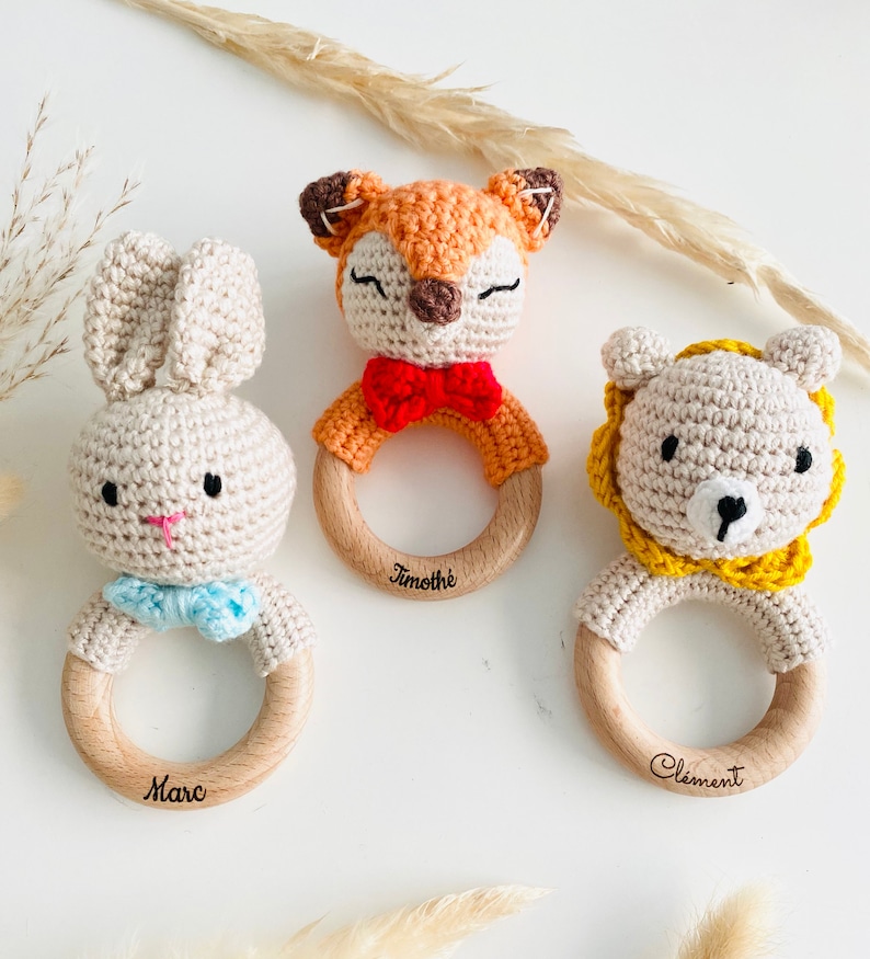 May include: Three wooden baby teethers with crocheted animal heads. The teethers are personalized with the names "Marc", "Timoth&eacute;e", and "Clement". The animals are a fox, a bunny, and a lion.