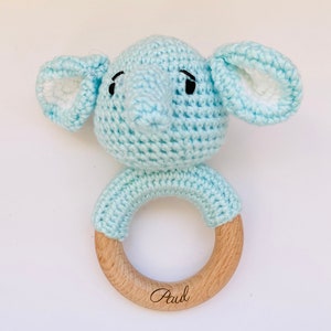 May include: A light blue crocheted elephant rattle with a wooden ring. The ring is engraved with the name "Paul".