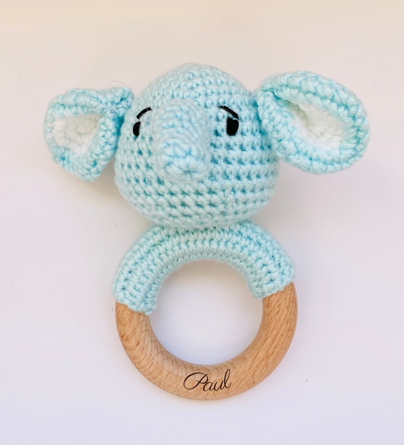 May include: A light blue crocheted elephant rattle with a wooden ring. The ring is engraved with the name "Paul".