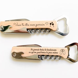 May include: Two wooden wine bottle openers with engraved sayings. The top opener says "Veux-tu &ecirc;tre mon parrain?" with a drawing of two wine glasses. The bottom opener says "Ne jamais boire le lendemain ce qu'on peut boire le jour m&ecirc;me" with a drawing of two wine glasses.