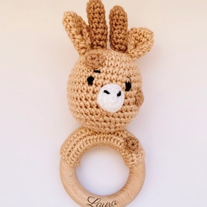 May include: A crocheted giraffe rattle with a wooden ring. The ring is engraved with the name "Laura".
