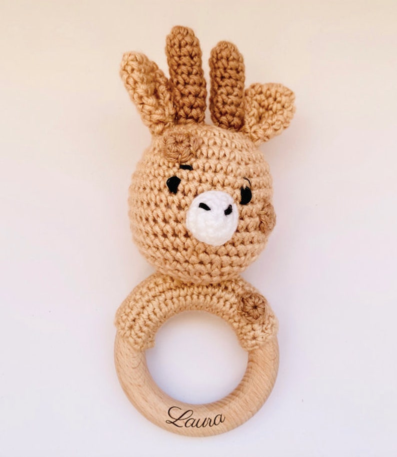 May include: A crocheted giraffe rattle with a wooden ring. The ring is engraved with the name "Laura".
