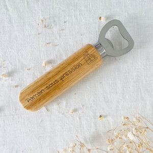 May include: Wooden bottle opener with a silver metal top. The handle is engraved with the text "Parrain sous pression".