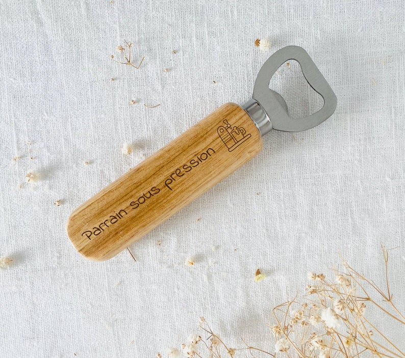 May include: Wooden bottle opener with a silver metal top. The handle is engraved with the text "Parrain sous pression".