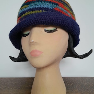 Puede incluir: Un gorro de punto azul y multicolor con un ala ancha. El gorro está en una cabeza de maniquí.