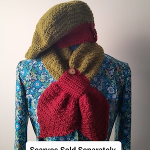Puede incluir: Boina de ganchillo verde oliva hecha a mano con una banda roja y bufanda a juego. La bufanda es de color rojo intenso y se abrocha con un botón de madera. El texto "Scarves Sold Separately" está en la parte inferior de la imagen.