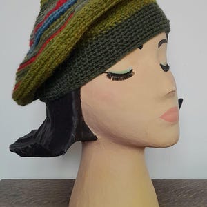 Puede incluir: Un gorro verde con un patrón de rayas multicolores. El gorro está hecho de lana tejida y tiene una parte superior puntiaguda.