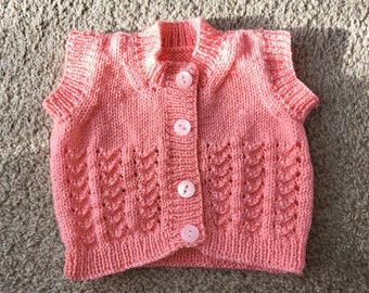 Hand knitted baby waistcoat / body warmer in soft blush pink wool in a cute pattern with matching buttons