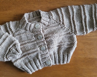 Hand knitted baby cardigan in soft beige wool. Elaborate pattern with matching beige buttons.