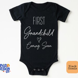 May include: Black onesie with white text that reads "First Grandchild Coming Soon" with a heart symbol.
