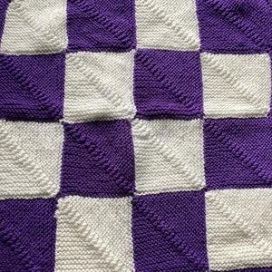 Peut inclure: Une couverture à carreaux avec des carrés alternés de tissu blanc et violet tricoté. Le tissu a un motif texturé.
