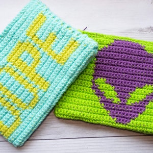 May include: Two crocheted pouches, one light blue with yellow lettering that says "Hello" and one green with a purple alien skull design.