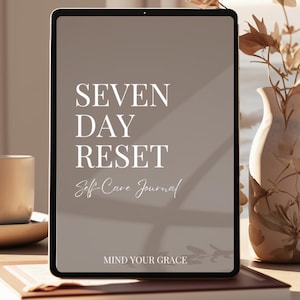 Puede incluir: Una tableta digital que muestra un diario de autocuidado titulado "Seven Day Reset Self-Care Journal" con el texto "Mind Your Grace" en la parte inferior de la pantalla.