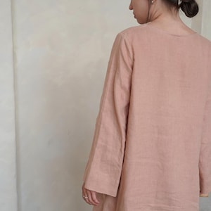 Pode incluir: Um vestido longo de linho cor de rosa. O vestido tem um corte folgado com decote redondo e mangas largas. O tecido parece leve e respir&aacute;vel, adequado para climas mais quentes. O vestido &eacute; de cor lisa com um design simples e elegante.