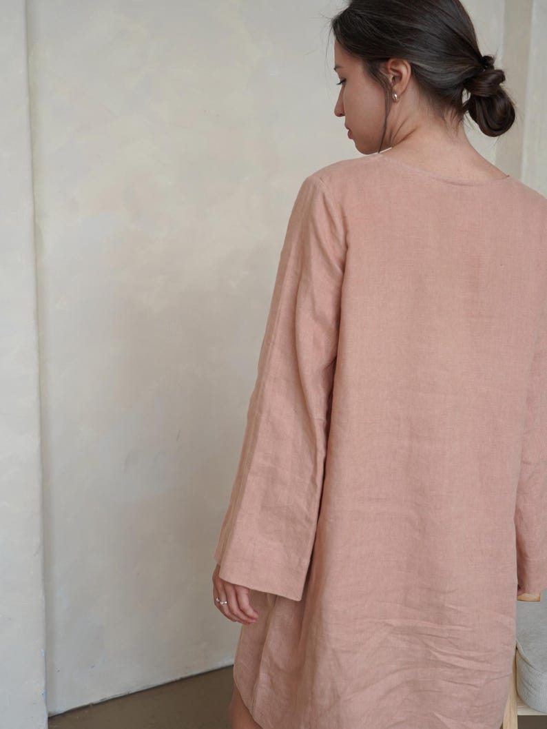 Pode incluir: Um vestido longo de linho cor de rosa. O vestido tem um corte folgado com decote redondo e mangas largas. O tecido parece leve e respir&aacute;vel, adequado para climas mais quentes. O vestido &eacute; de cor lisa com um design simples e elegante.