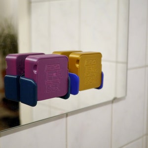 May include: Two small, square-shaped boxes with different colored designs. The box on the left is purple with a blue base and the box on the right is gold with a blue base.