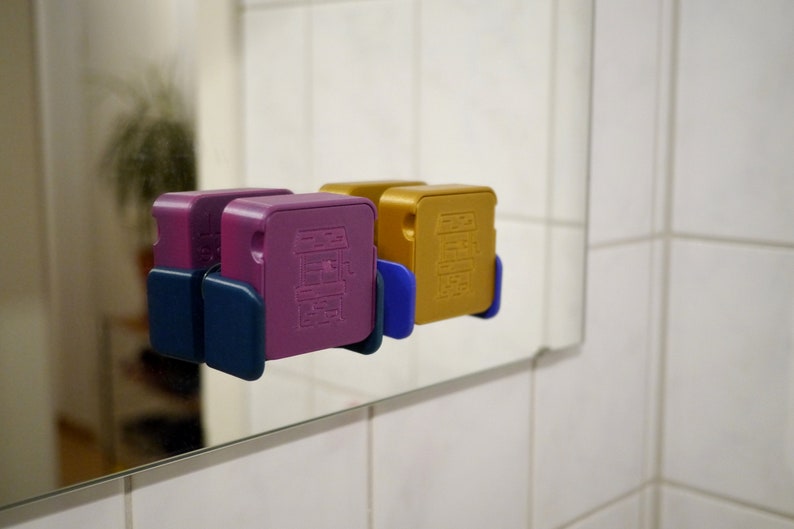 May include: Two small, square-shaped boxes with different colored designs. The box on the left is purple with a blue base and the box on the right is gold with a blue base.