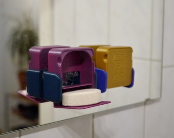 May include: Two 3D printed soap dispensers, one purple and one gold, with a white soap tablet in the purple dispenser. The dispensers have a blue accent on the side.
