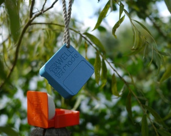 May include: A blue square-shaped object with the text "WELL MADE" hanging from a branch with a rope. The object is attached to a smaller orange object.