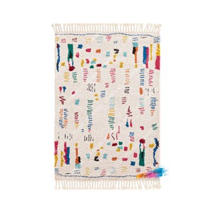 May include: A white rug with a colorful geometric pattern. The rug has a fringe border and is made of wool.