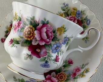 May include: White teacup and saucer set with a floral design featuring pink, yellow, and blue flowers. The cup and saucer have a scalloped edge and gold trim. A classic tea set.