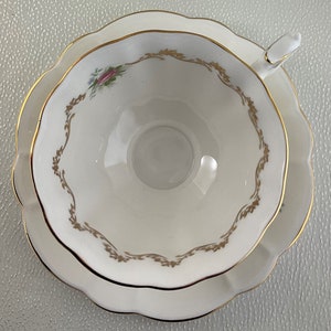 May include: A white teacup and saucer set with a scalloped edge and gold trim. The teacup features a delicate floral design and gold filigree. The saucer mirrors the teacup's shape and design, creating a cohesive set.