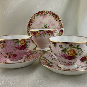 May include: A set of vintage teacups and saucers. The cups and saucers are decorated with a pink floral pattern and gold trim. The set includes two teacups, two saucers, and a small teacup with a matching saucer.