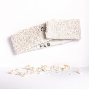Może przedstawiać: Jasnoszary opaska do włosów o miękkiej, puszystej fakturze. Opaska ma mały guzik i etykietę z napisem "DSR". Opaska jest otoczona białymi perełkami i muszelkami.