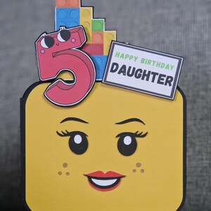 May include: A yellow Lego-themed birthday card featuring a smiling face, a red number 5, and colourful Lego bricks. The card includes a sign that reads "HAPPY BIRTHDAY DAUGHTER".