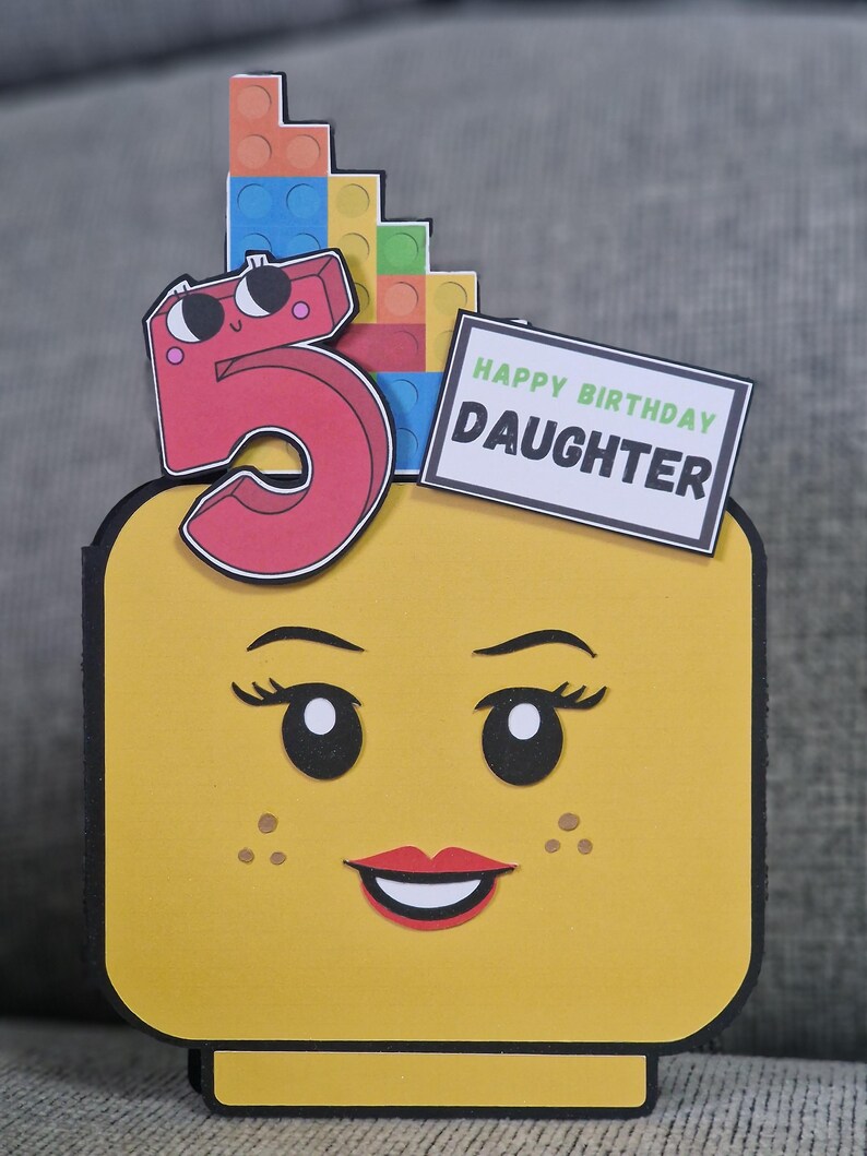 May include: A yellow Lego-themed birthday card featuring a smiling face, a red number 5, and colourful Lego bricks. The card includes a sign that reads "HAPPY BIRTHDAY DAUGHTER".