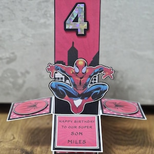 May include: A handmade birthday card with a Spider-Man theme. The card is red and black with a pop-up design. It features the number 4, a Spider-Man graphic, and the text "Happy Birthday to our Super Son Miles."