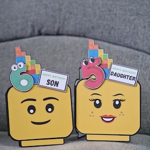 May include: Two yellow Lego-style birthday cards. One card has a green number 6 and says "Happy Birthday Son". The other card has a pink number 5 and says "Happy Birthday Daughter". Both cards have colourful block accents.