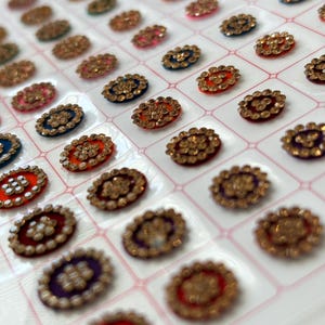May include: A sheet of adhesive rhinestones in various colors and designs. The rhinestones are arranged in a grid pattern on a white background.