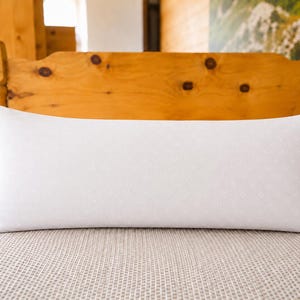 Könnte beinhalten: Ein rechteckiges weißes Nackenkissen mit einem dezenten, sich wiederholenden geometrischen Muster auf der Oberfläche. Das Kissen hat eine glatte, saubere Oberfläche und ist horizontal ausgerichtet, was seine längliche Form unterstreicht.
