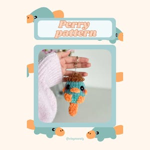 May include: A handmade crochet Perry the Platypus keychain. The keychain is blue, orange, and brown, with a small hat. The image also includes the text "Perry pattern".