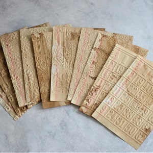 May include: A collection of vintage paper ephemera with embossed designs. The aged papers feature floral patterns, alphabet letters, and bingo cards. The papers have a sepia tone with red vertical lines.