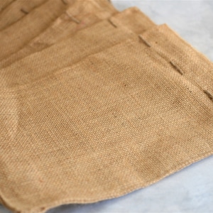 May include: A stack of brown burlap bags with a rough texture. The bags are folded and have a seam along the top edge.