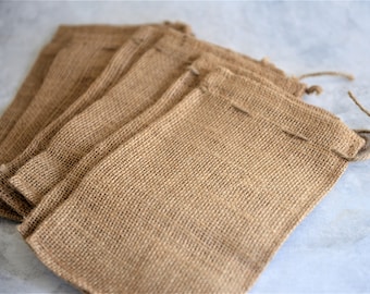 May include: A stack of six brown burlap bags with drawstrings. The bags are made of a coarse, woven fabric and are perfect for packaging small items.