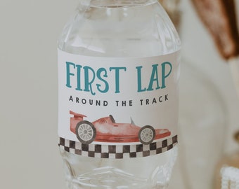 Può includere: Una bottiglia d'acqua in plastica trasparente con un'etichetta bianca che dice "First Lap Around The Track". L'etichetta presenta un'auto da corsa rossa con un design a scacchi blu e bianco. La bottiglia è appoggiata su un sottobicchiere di legno.