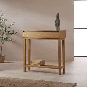 May include: A light oak console table with a drawer and a lower shelf. A small cactus in a grey pot sits on top. A small wooden box rests on the shelf below. The table is made of light-coloured wood.